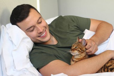Yakışıklı genç adamın yakın plan portresi evde kedisiyle yatakta dinleniyor.