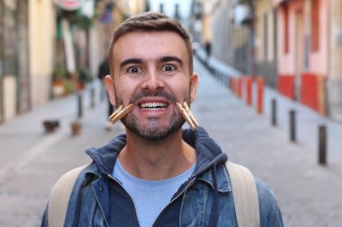 Yüzünde mandallarla sokakta somurtan yakışıklı bir gencin yakın plan portresi.