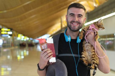 Kedisiyle seyahat eden ve tren istasyonunda duran yakışıklı bir gencin yakın plan portresi.