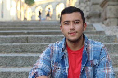 Ekose gömlekli, merdivenlerde oturan yakışıklı genç adamın yakın plan portresi.