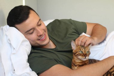 Yakışıklı genç adamın yakın plan portresi evde kedisiyle yatakta dinleniyor.