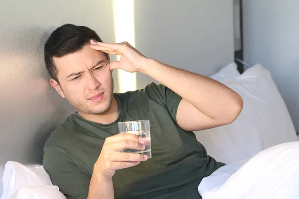 close-up portrait of handsome young man with headache drinking water in bed at home
