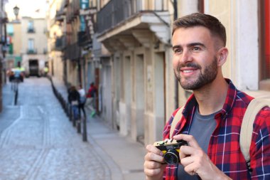 Eski şehir caddesinde sırt çantalı ve klasik kameralı yakışıklı bir gencin yakın plan portresi.