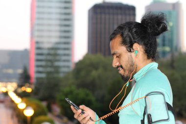 close-up portrait of handsome young mixed race man in sportswear with water bottle and earphones on street