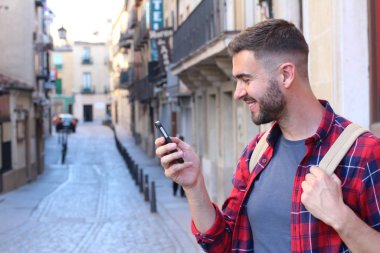 Eski şehir caddesinde akıllı telefon kullanan sırt çantalı yakışıklı bir gencin yakın plan portresi.