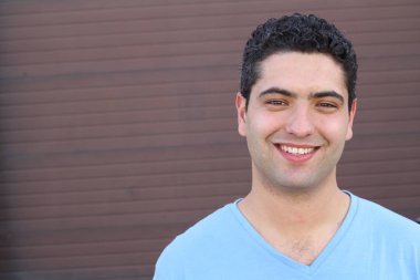 close-up portrait of handsome young man in blue t-shirt in front of brown wall