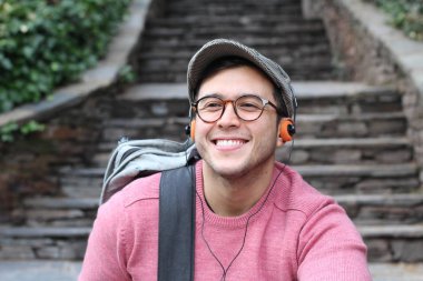 Yakından çekilmiş bir portre, günlük giysiler içindeki yakışıklı genç adam klasik kulaklıklarla müzik dinliyor ve şehir sokaklarında oyuncu.