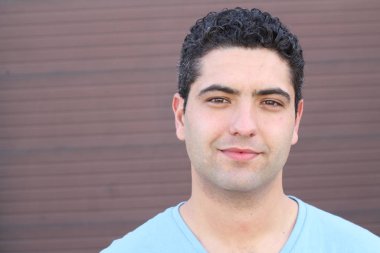 close-up portrait of handsome young man in blue t-shirt in front of brown wall