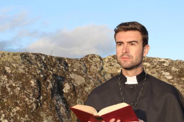 Doğada İncil 'i olan yakışıklı genç bir rahibin yakın plan portresi.