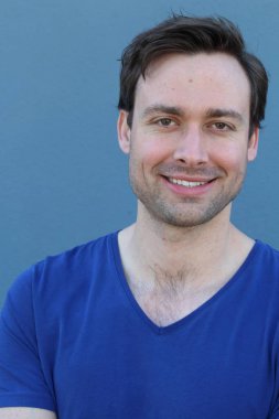 Mavi duvarın önünde sıradan giyinmiş yakışıklı bir gencin yakın plan portresi.