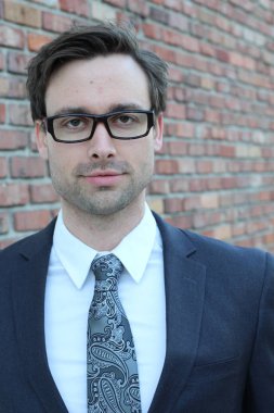 Tuğla duvarın önünde yakışıklı genç işadamının yakın plan çekimi.