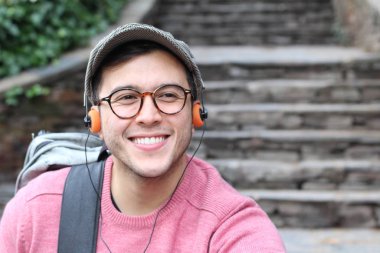 Yakından çekilmiş bir portre, günlük giysiler içindeki yakışıklı genç adam klasik kulaklıklarla müzik dinliyor ve şehir sokaklarında oyuncu.