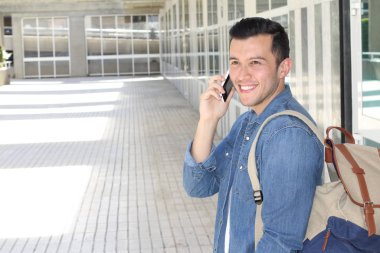 Sokakta telefonla konuşan, günlük kıyafetler içindeki yakışıklı genç adamın yakın plan portresi.