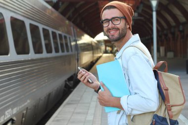 Yakından bakınca, tren istasyonunda akıllı telefonlu sıradan giysili yakışıklı bir gencin portresi.