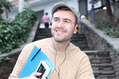 Yakından çekilmiş bir portre, günlük giysiler içindeki yakışıklı genç adam klasik kulaklıklarla müzik dinliyor ve şehir sokaklarında oyuncu.