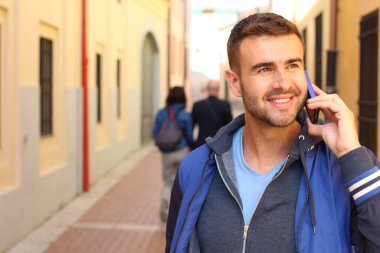Sokakta telefonla konuşan, günlük kıyafetler içindeki yakışıklı genç adamın yakın plan portresi.