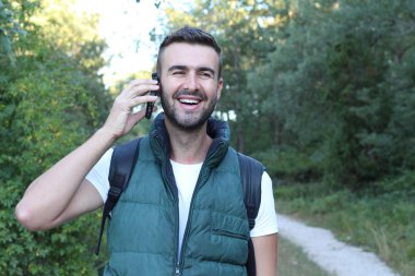 Doğada telefonla konuşan yakışıklı genç adamın yakın plan portresi.