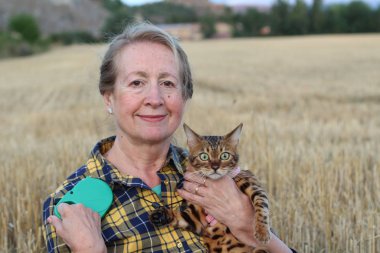 Yaşlı kadın elinde şirin bir kedi tutuyor, gündüzleri kuru tarlada duruyor. 