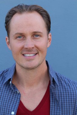 Mavi duvarın önünde sıradan giyinmiş yakışıklı bir gencin yakın plan portresi.