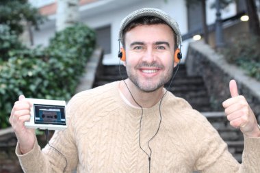 Yakından çekilmiş bir portre, günlük giysiler içindeki yakışıklı genç adam klasik kulaklıklarla müzik dinliyor ve şehir sokaklarında oyuncu.