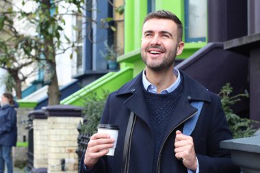 Sokakta elinde kağıt bardak kahveyle ceketli yakışıklı bir gencin yakın plan portresi.