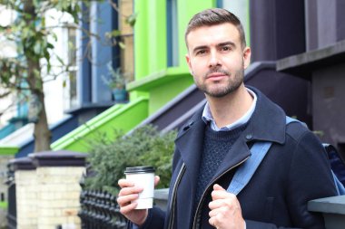 Sokakta elinde kağıt bardak kahveyle ceketli yakışıklı bir gencin yakın plan portresi.
