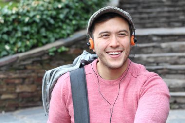 Yakından çekilmiş bir portre, günlük giysiler içindeki yakışıklı genç adam klasik kulaklıklarla müzik dinliyor ve şehir sokaklarında oyuncu.