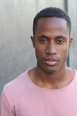 Gri duvarın önünde pembe tişörtlü yakışıklı genç adamın yakın plan portresi.