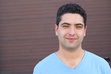 close-up portrait of handsome young man in blue t-shirt in front of brown wall