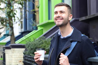 Sokakta elinde kağıt bardak kahveyle ceketli yakışıklı bir gencin yakın plan portresi.