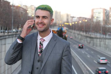 Şık, yakışıklı, yeşil saçlı adam şehirde telefonla konuşuyor.