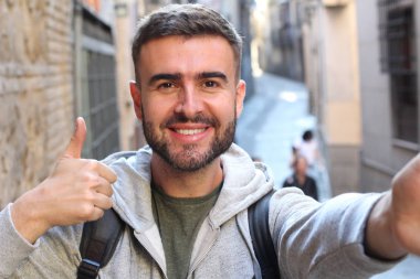 close-up portrait of handsome young man showing thumb up at camera on street