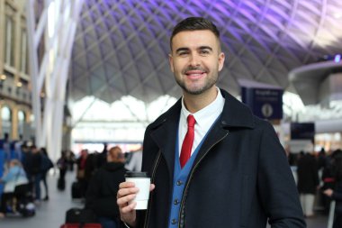 Takım elbiseli ve ceketli yakışıklı genç işadamının kağıt bardak kahveyle yakın plan portresi.