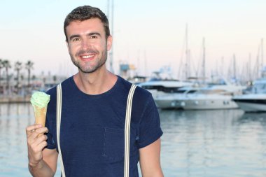 Gün batımında yatların önünde limanda dondurma yiyen şık elbiseli yakışıklı bir gencin yakın plan portresi. 