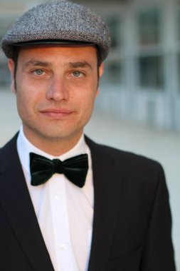 Siyah takım elbiseli, papyonlu ve şapkalı yakışıklı bir adamın yakın plan portresi.