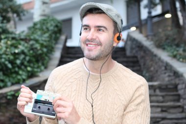 Yakından çekilmiş bir portre, günlük giysiler içindeki yakışıklı genç adam klasik kulaklıklarla müzik dinliyor ve şehir sokaklarında oyuncu.