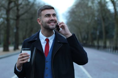 Takım elbiseli ve ceketli yakışıklı genç işadamının kağıt bardak kahveyle yakın plan portresi.