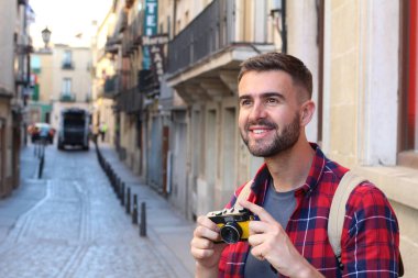 Eski şehir caddesinde sırt çantalı ve klasik kameralı yakışıklı bir gencin yakın plan portresi.