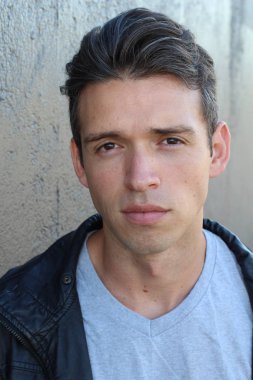 Gri duvarın önünde sıradan giyinmiş yakışıklı bir gencin yakın plan portresi.