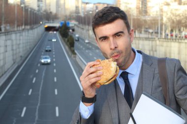 close-up portrait of handsome young businessman in suit eating burger on street
