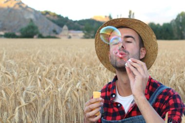 Çiftçi elbiseli yakışıklı genç adamın yakın plan portresi doğaya sabun köpüğü üflüyor.