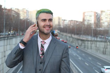 Şık, yakışıklı, yeşil saçlı adam şehirde telefonla konuşuyor.