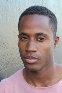 Gri duvarın önünde pembe tişörtlü yakışıklı genç adamın yakın plan portresi.