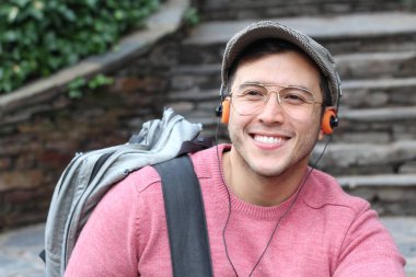 Yakından çekilmiş bir portre, günlük giysiler içindeki yakışıklı genç adam klasik kulaklıklarla müzik dinliyor ve şehir sokaklarında oyuncu.