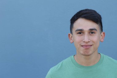 Mavi duvarın önündeki yeşil tişörtlü yakışıklı genç adamın yakın plan portresi.