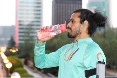 close-up portrait of handsome young mixed race man in sportswear with water bottle and earphones on street