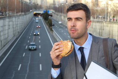 close-up portrait of handsome young businessman in suit eating burger on street