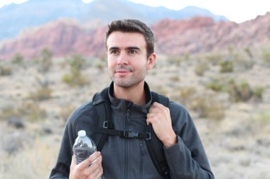 Sırt çantalı ve arka planda bir şişe su olan gülümseyen adam.