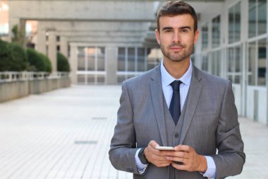 Yakışıklı, zarif bir adam gülümsüyor ve elinde akıllı telefon tutuyor.