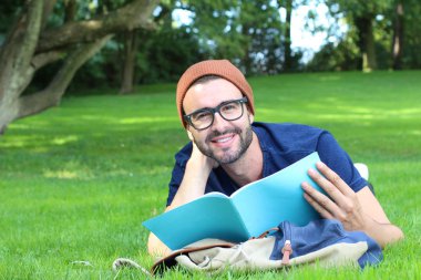 Çimlerin üzerinde yatarken not defteriyle çalışan yakışıklı bir gencin yakın plan portresi.